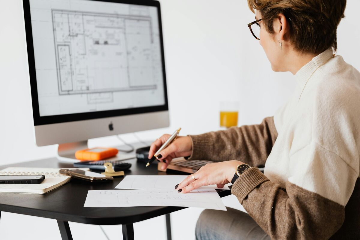 Frau am Rechner von der Seite, auf dem Monitor sind digitale Grundrisspläne sichtbar – moderne Immobilienplanung und digitales Projektmanagement.